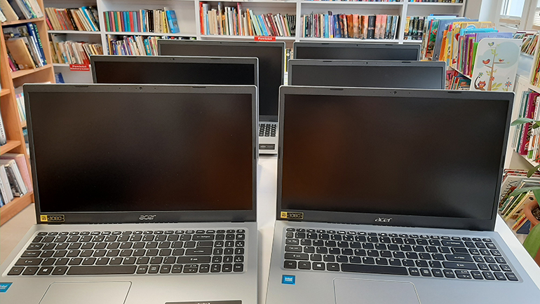 Na zdjęciu widać sześć laptop&oacute;w na stoliku w tle regał z książkami
