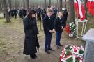 trzy osoby stoją z pochyloną głową w dół przed pomnikiem