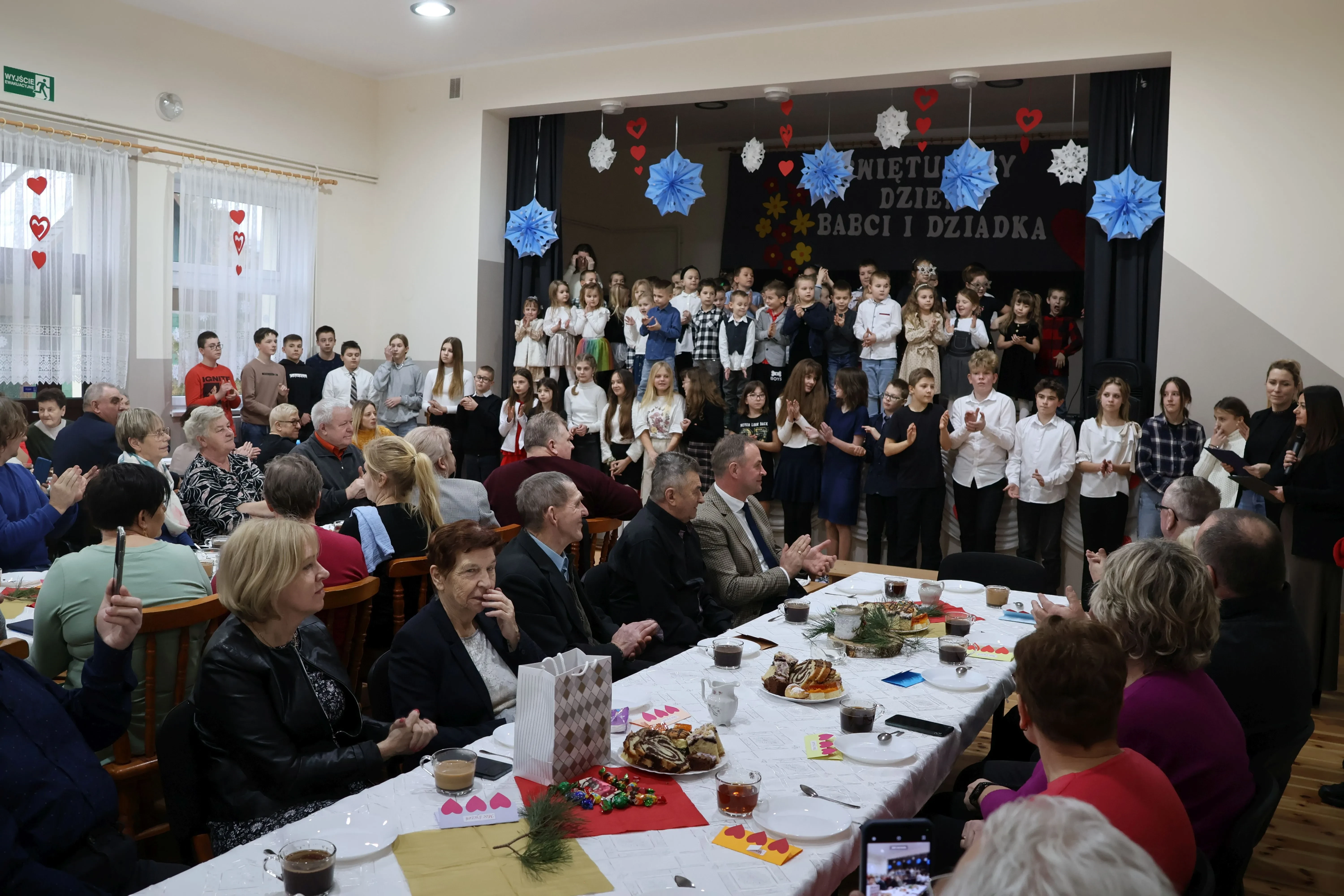zebrani na sali, w tle uczniowie na scenie