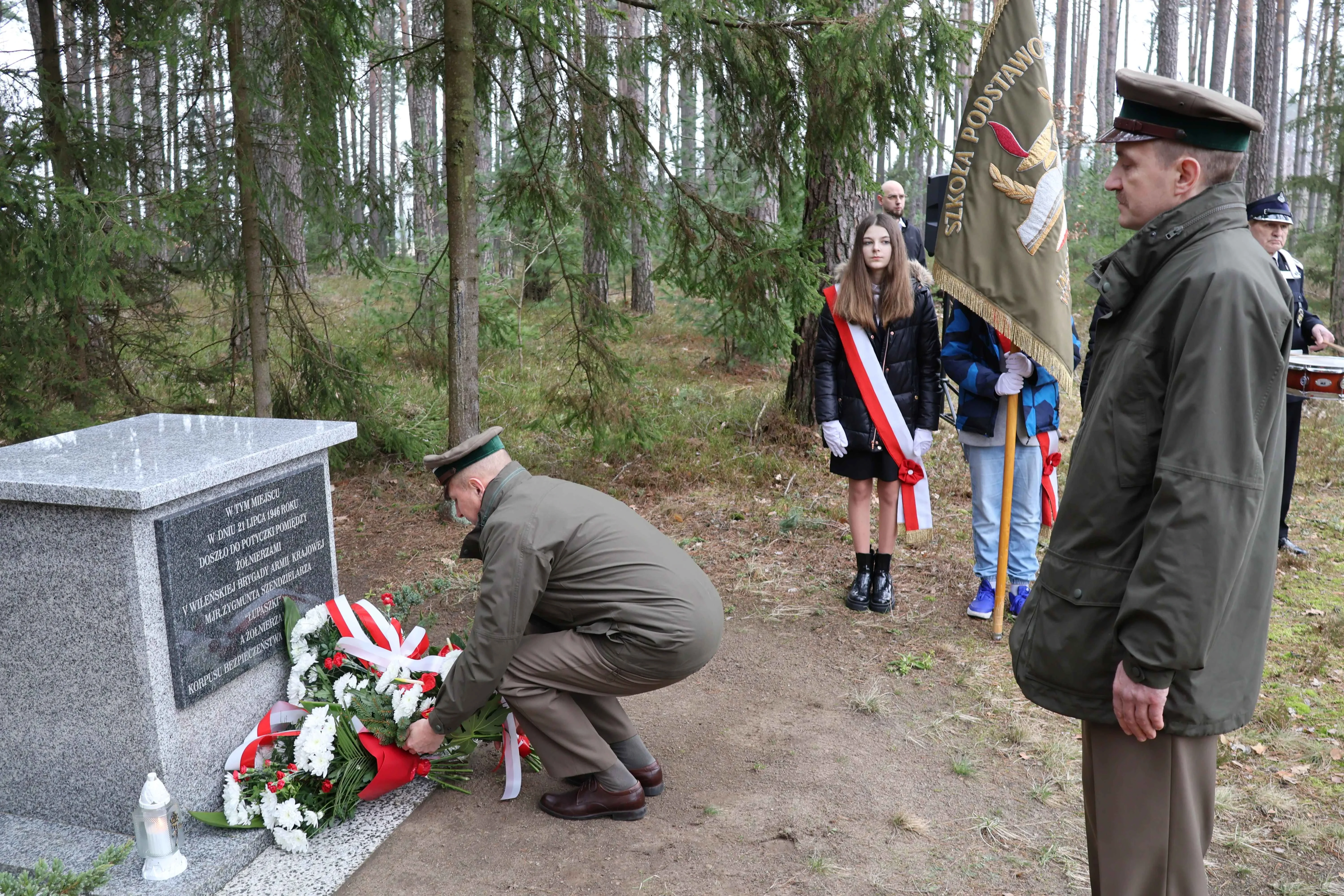 wojskowy składa bukiet kwiatów pod pomnikiem
