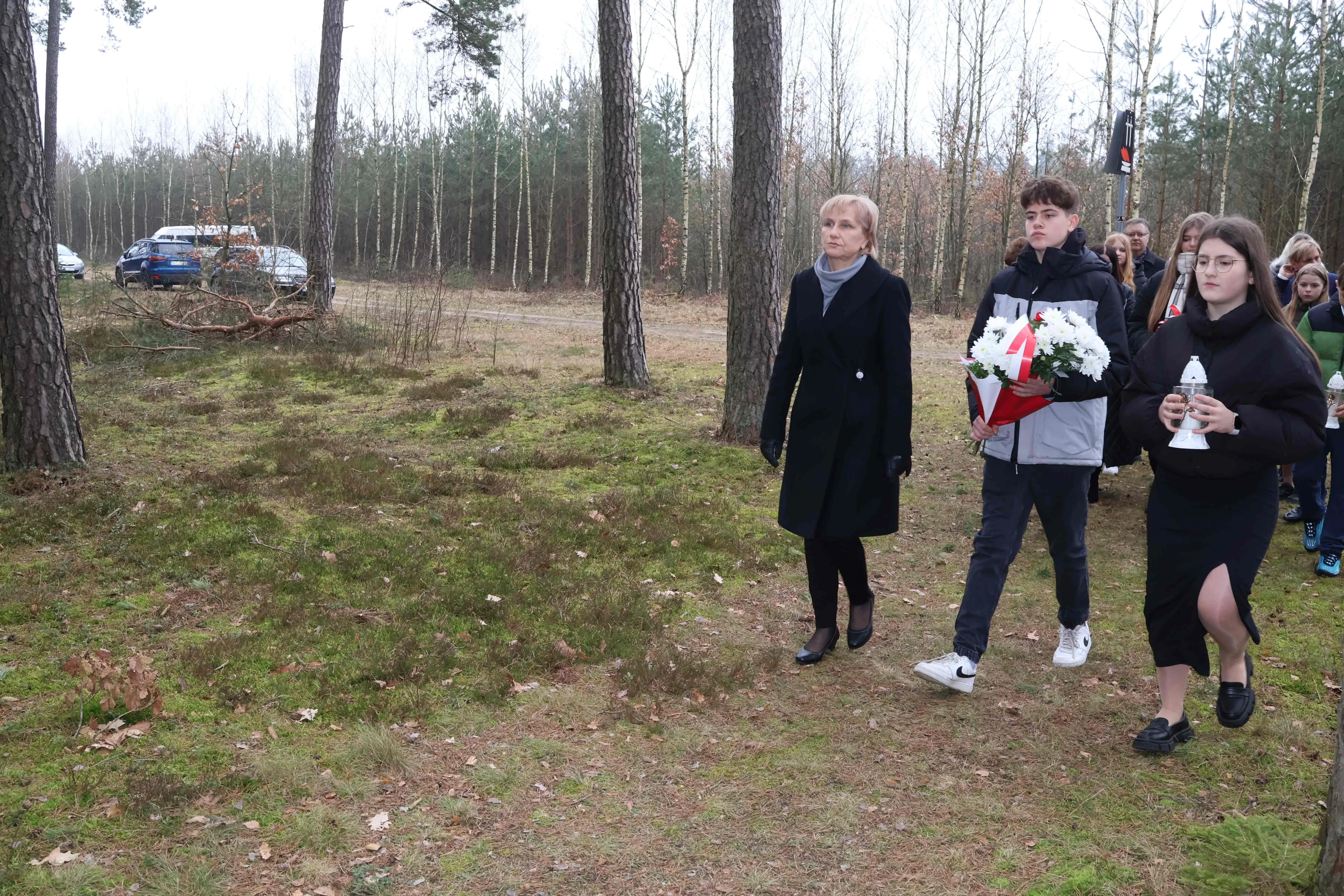 dwójka dzieci trzyma bukiet kwiatów i znicz