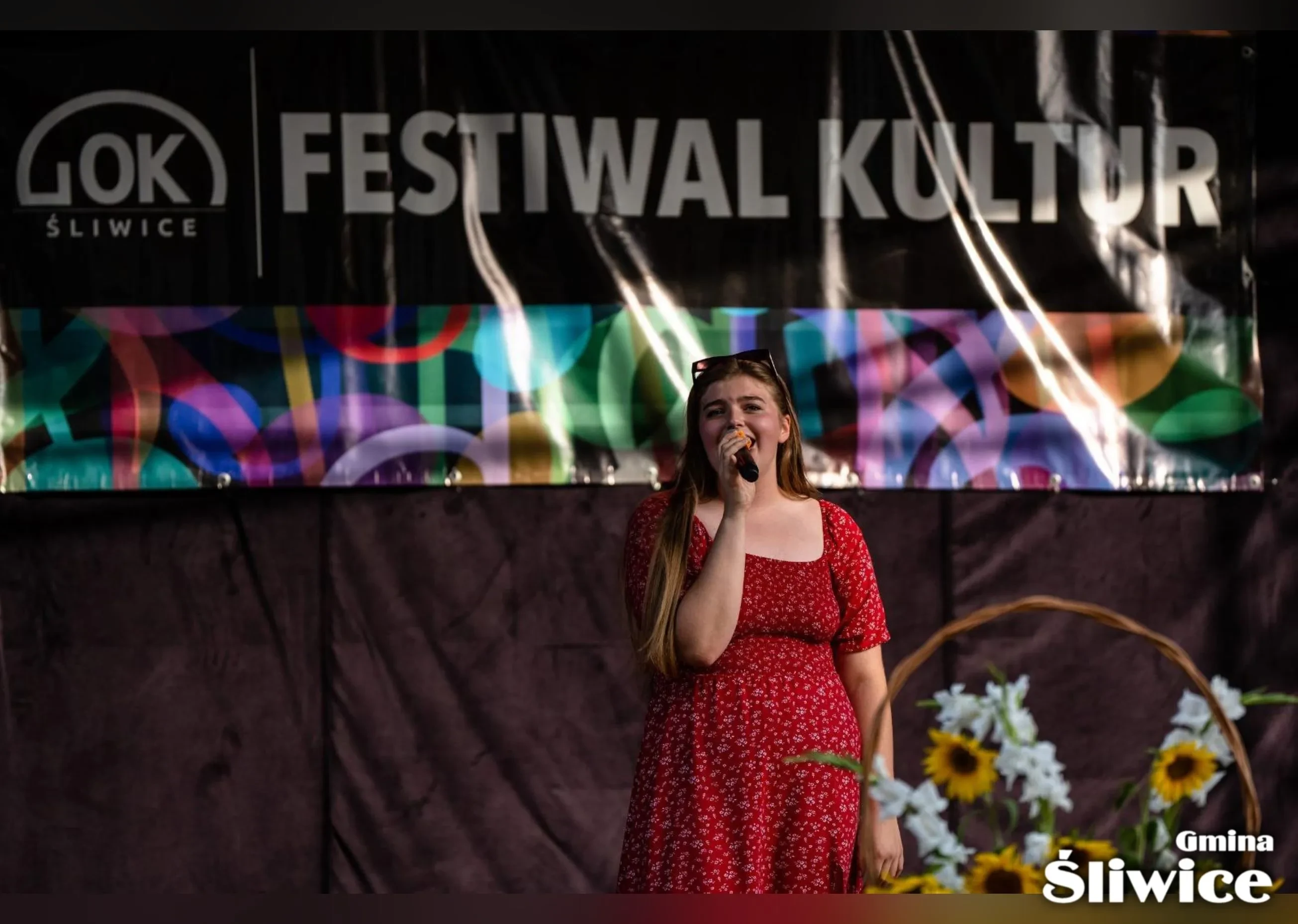 kobieta w czerwonej sukience śpiewa na scenie w tle baner festiwal kultur