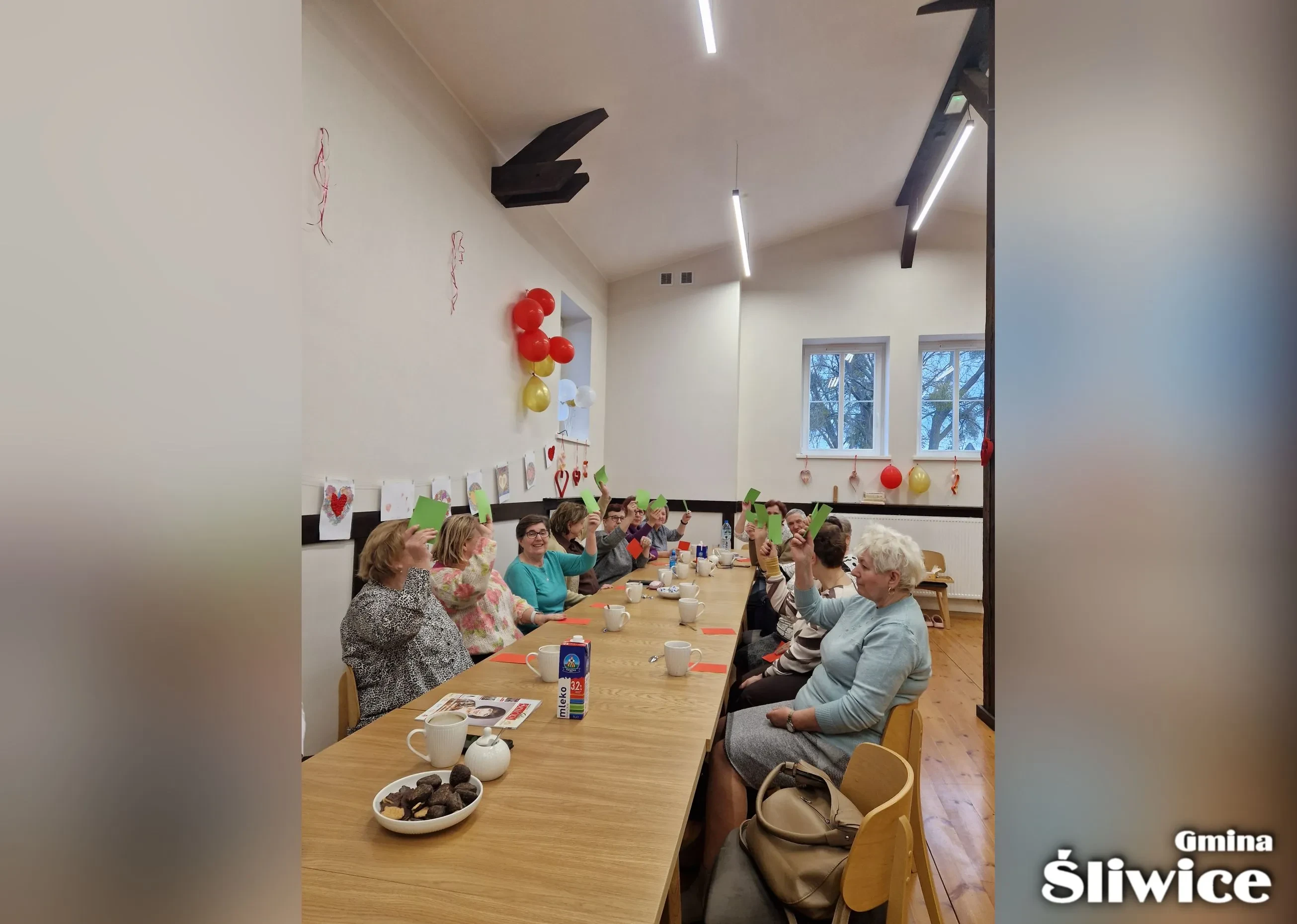 zebrani przy stołach podnoszą kartki w górę